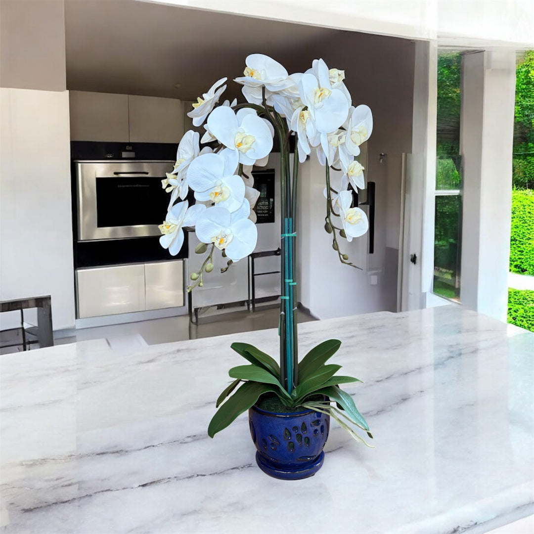 White orchid artificial flowers arranged in a decorative blue ceramic planter