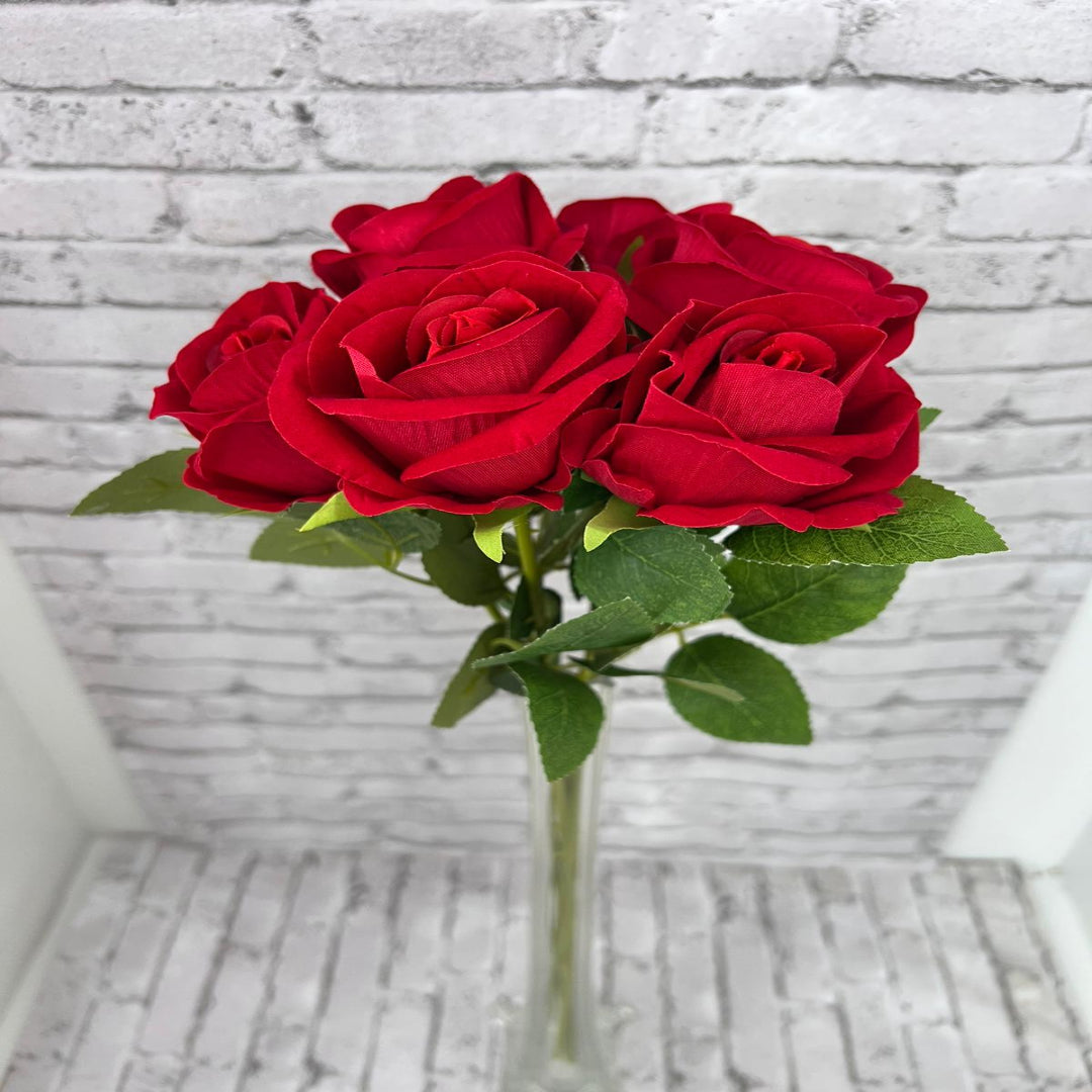 Close up of blooming artificial red roses arranged in glass vase